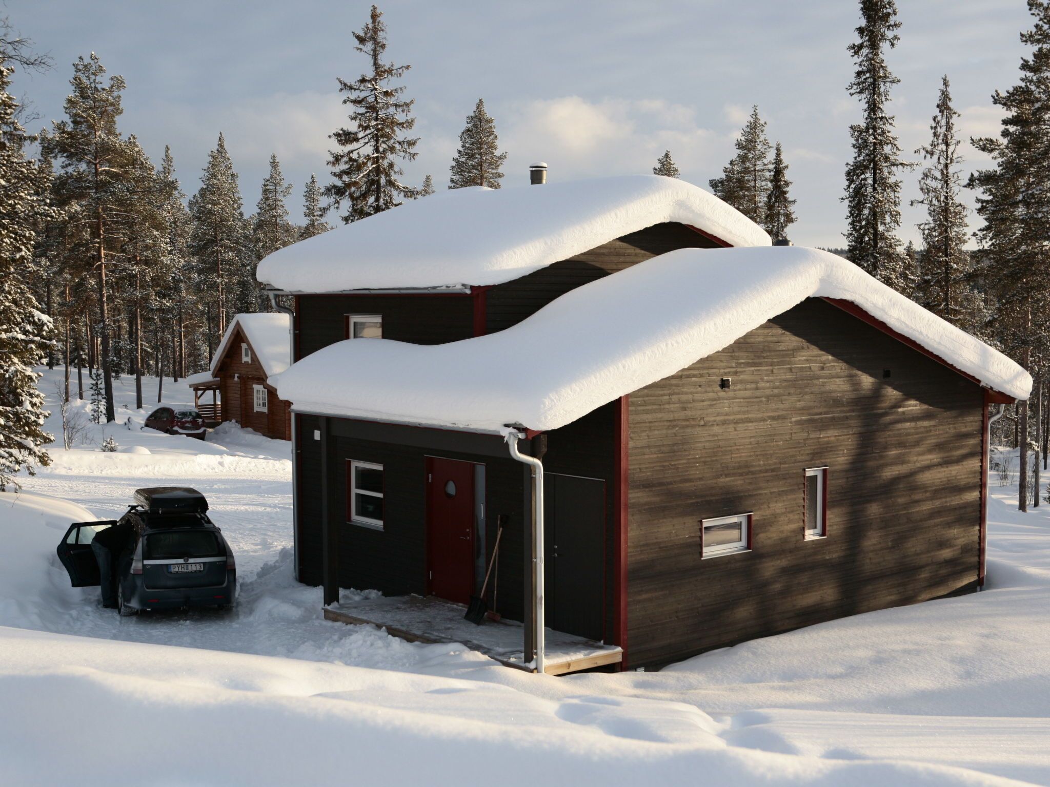 Una cabaña con garaje, rodeada de árboles cubiertos de nieve.