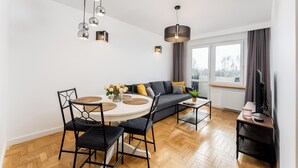 Una sala de estar moderna con comedor, un sofá con cojines, un televisor y una ventana con cortinas.