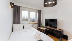 Una habitación de hotel moderna con una cama grande, un televisor de pantalla plana, un escritorio con una planta y vistas a la ciudad a través de la ventana.