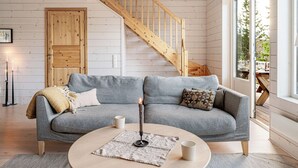 Una sala acogedora con un sofá gris, una mesa redonda de centro y una escalera de madera.