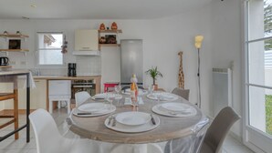 A modern kitchen with white cabinets, a wooden dining table set with white plates and glasses, and a giraffe decoration on the wall. - Le Bas d'Anville by Interhome (Etaules)