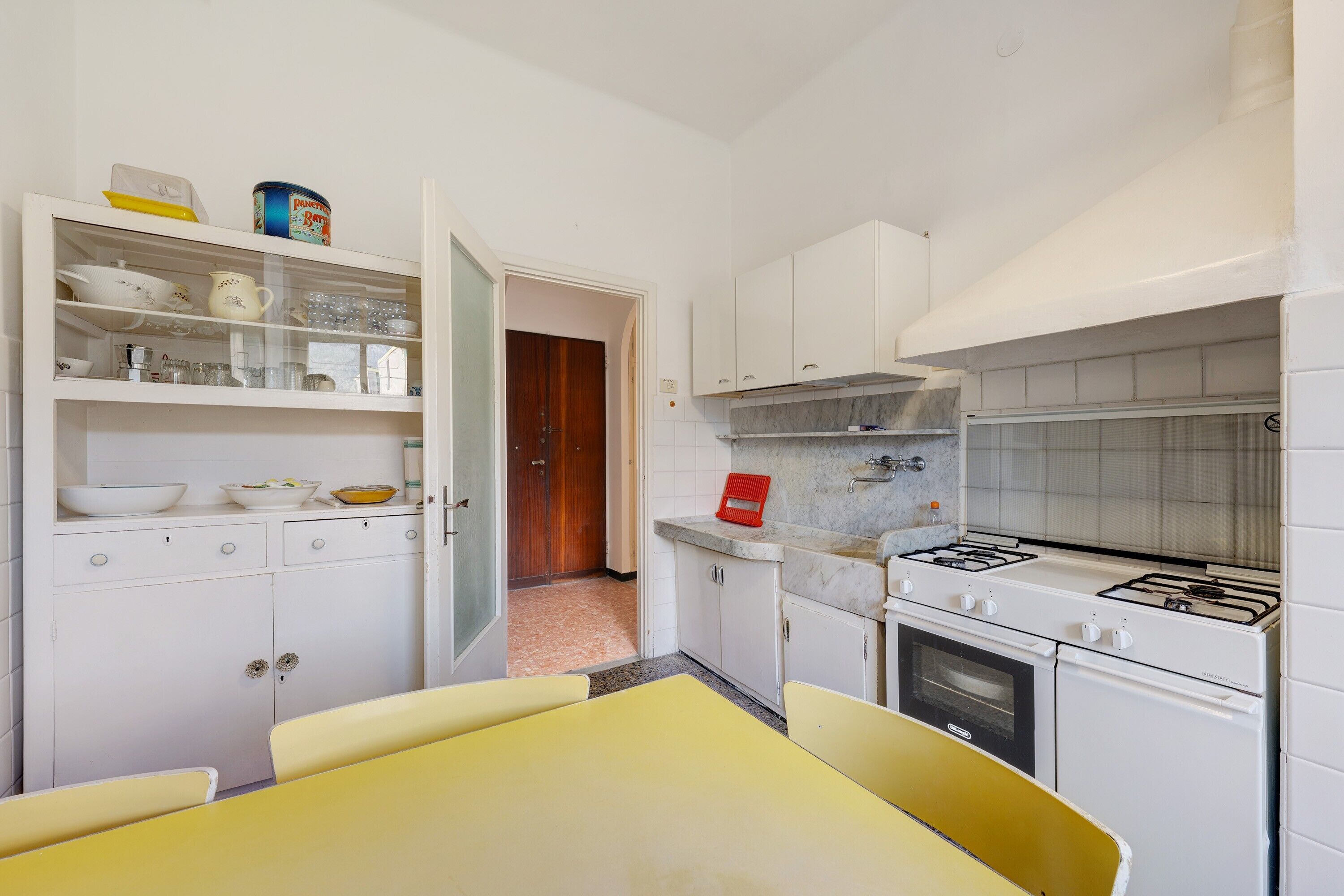 Une cuisine de taille réduite avec des meubles blancs, une table jaune et une cuisinière.