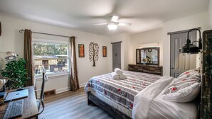 A bedroom with a bed, desk, and chair, a window with curtains, a ceiling fan, and a dresser. - The Nest:A Sanctuary of Nature & Luxury (Charlotte)