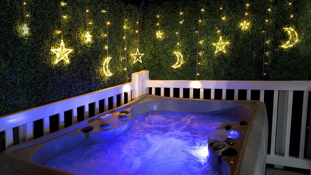A hot tub with a white railing, surrounded by a lush green wall with star and moon decorations. - The Nest:A Sanctuary of Nature & Luxury (Charlotte)