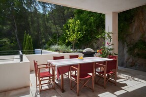 Un patio al aire libre con una mesa y sillas, rodeado de follaje y vistas a árboles.