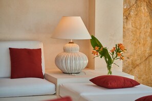Una habitación de hotel moderna con un sofá blanco, una lámpara blanca y un jarrón con flores.