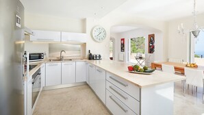 Une cuisine moderne avec des meubles blancs, un îlot central, une horloge et un coin repas offrant une vue agréable.