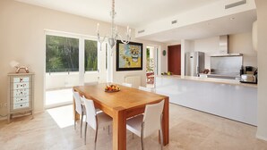 Une cuisine moderne avec une table et des chaises en bois, un réfrigérateur et un coin repas offrant une vue sur la verdure.