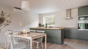 A modern kitchen with wooden floors, a dining area with white chairs, and a large window providing natural light. - Renen 6B by Interhome (Tännäskröket)
