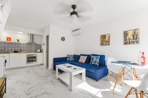 Un espace de vie moderne comprenant une cuisine, un canapé bleu, une table basse blanche et un coin repas avec une table ronde et des chaises.