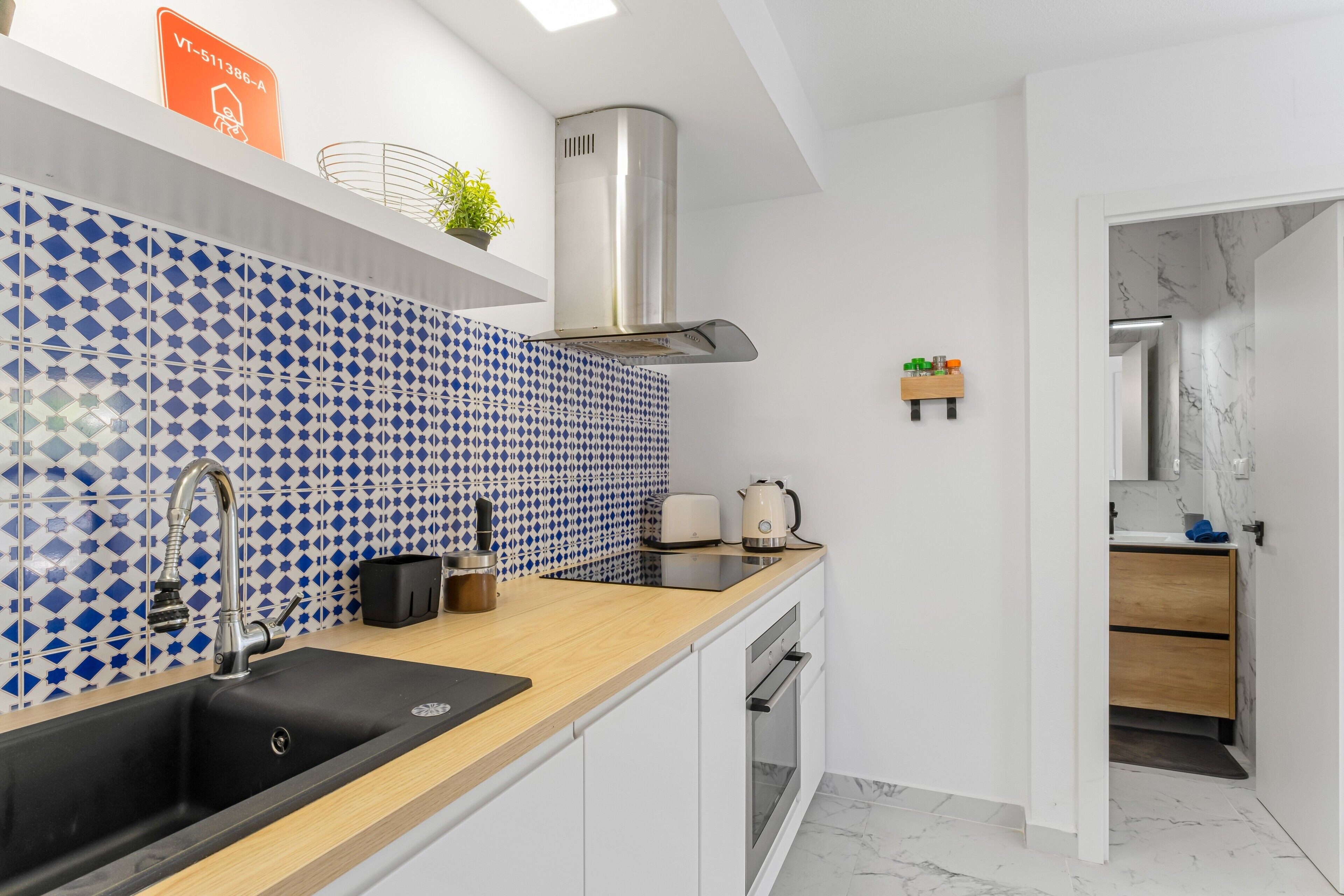 A modern kitchen with a black sink, stainless steel range hood, and a patterned backsplash.