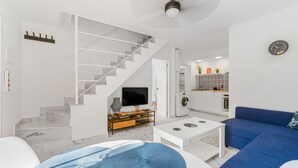 Een moderne woonkamer met een trap, een flatscreen televisie, een salontafel, een blauwe bank en een keuken in de achtergrond.