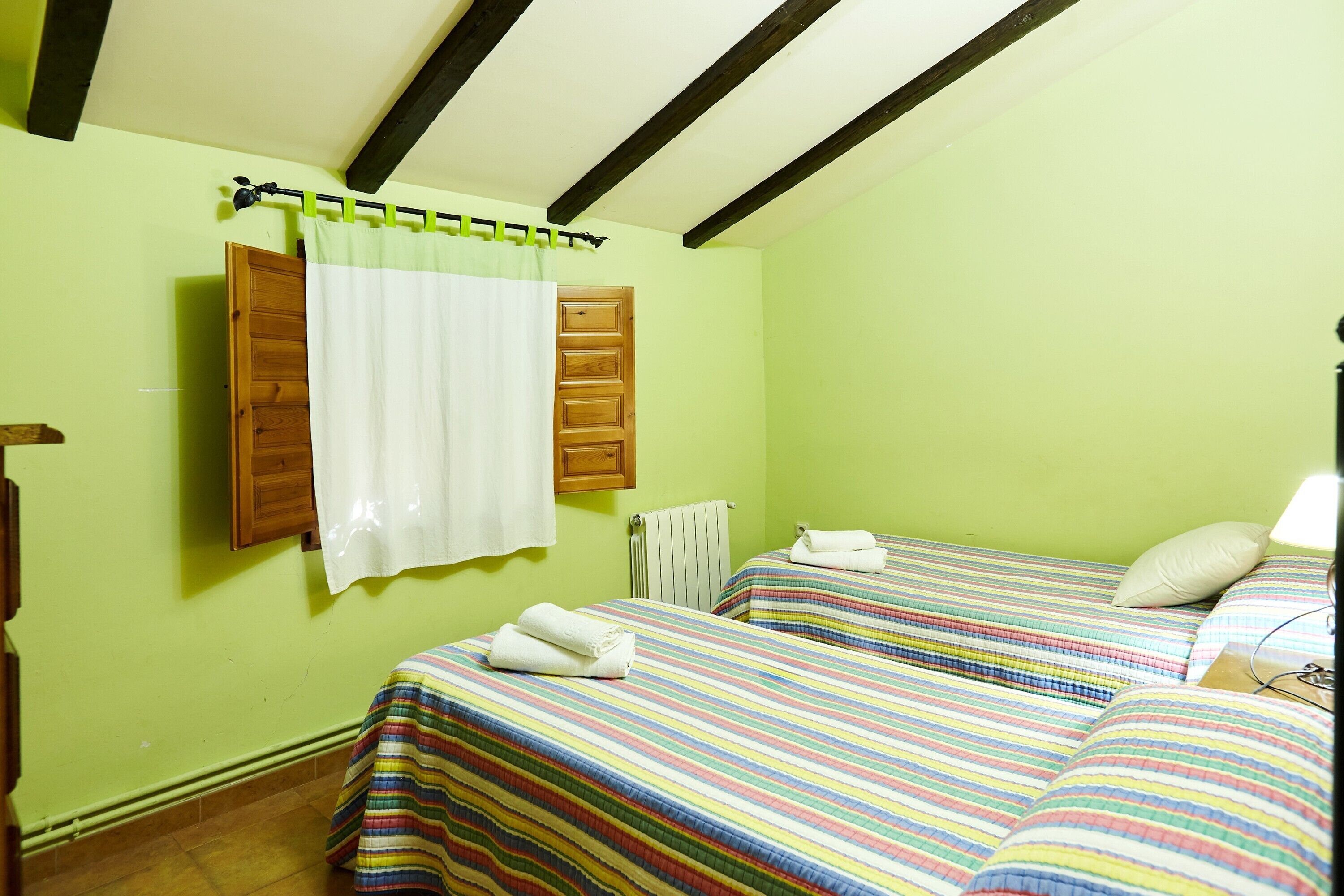 Una stanza con due letti, una porta in legno, una tenda bianca e un termosifone.