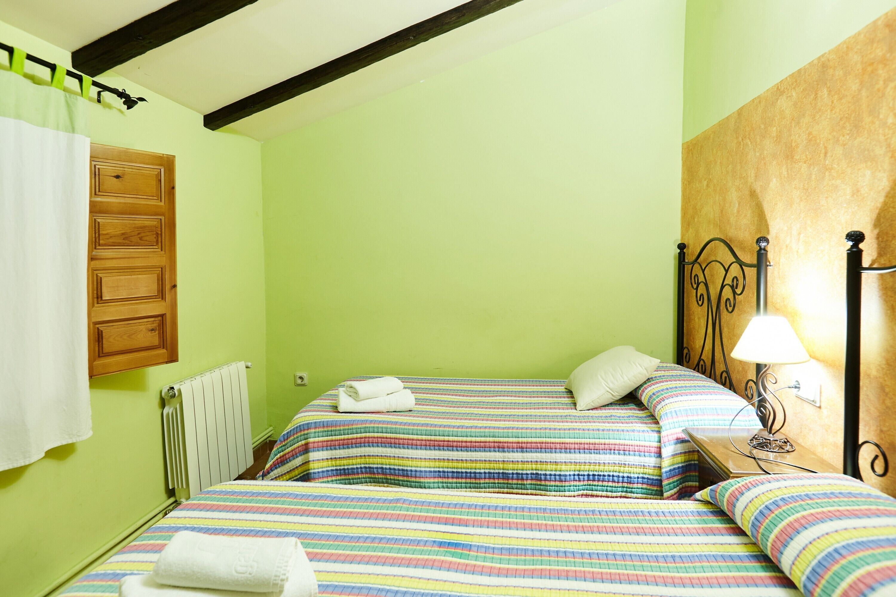 Una habitación con dos camas, un radiador, una puerta de madera y una mesita de noche con lámpara.