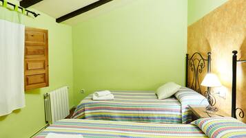 Una habitación con dos camas, un radiador, una puerta de madera y una mesita de noche con lámpara.