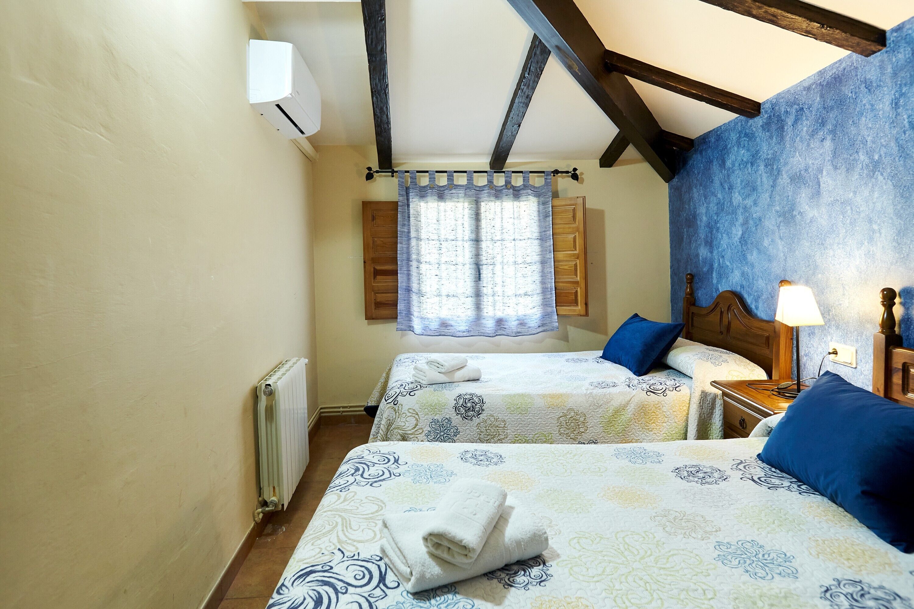Une chambre avec deux lits, un radiateur, une fenêtre avec des rideaux et une tête de lit en bois.