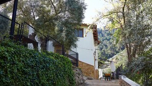 A narrow road leading to a white building with a stone base, surrounded by lush greenery and a mountainous backdrop. - Country House 'Los Angostones' with Mountain View, Pool and Air Conditioning (Villanueva Del Arzobispo)