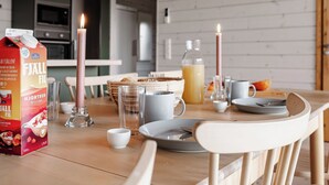 Een eettafel gedekt met borden, glazen, een kaars en een fruitsapverpakking in een moderne keuken met houten wanden en een houten stoel.
