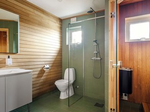 Ein modernes Badezimmer mit einer Wandpaneele aus Holz, einer Glaskabine für die Dusche, einer weißen Toilette und einem weißen Waschbecken.