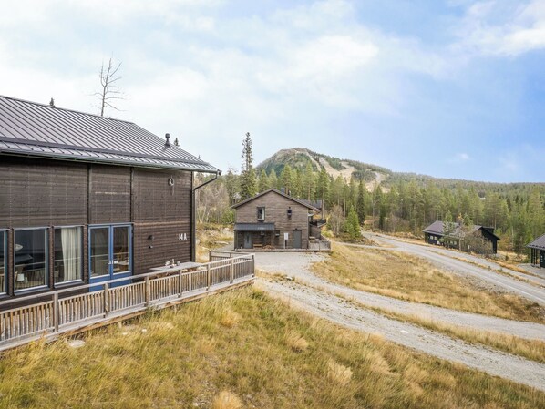 Una cabaña rústica con techo de metal, una terraza de madera y vista a una montaña boscosa.