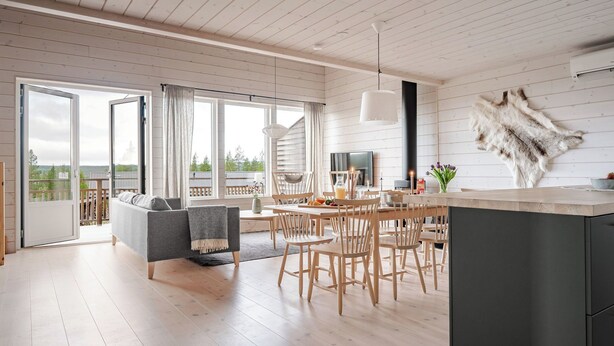 Een ruime woonkamer met een eettafel, stoelen en een bank. Een groot raam biedt uitzicht op de omgeving.