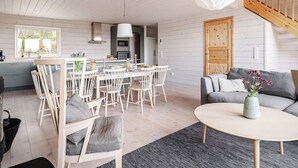 Een moderne keuken met witte kasten, een eethoek met houten stoelen, een grijze bank en een trap.