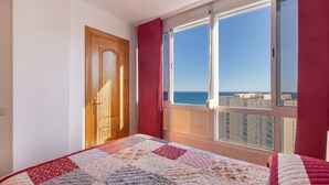 A bedroom with a large window, a wooden door, and a quilted bedspread.