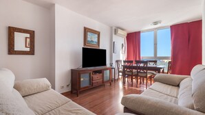 A living room with a flat-screen TV, wooden furniture, and a dining area with red curtains.