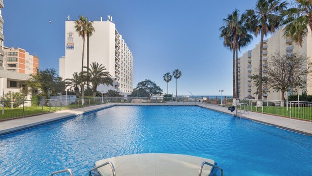 A swimming pool with a clear blue water, surrounded by tall buildings and palm trees.