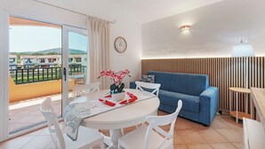 Un salon moderne avec une table ronde, des chaises blanches, un canapé bleu et un balcon offrant une vue sur les collines.