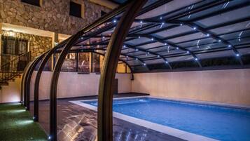 An indoor swimming pool with a stone wall and a covered area with a glass ceiling.
