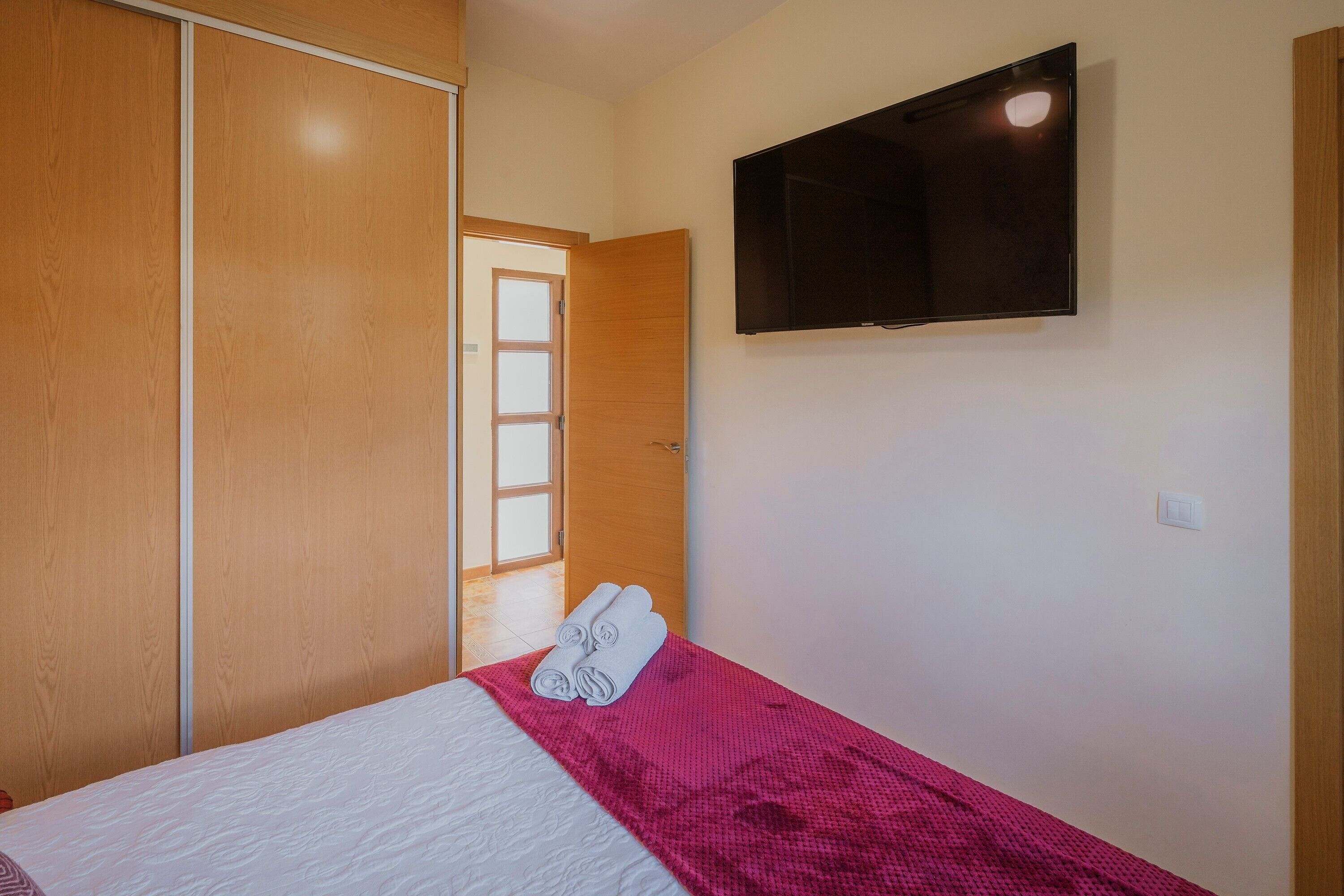 Ein Schlafzimmer mit einem Bett, einem an der Wand montierten Fernseher und einem Kleiderschrank.