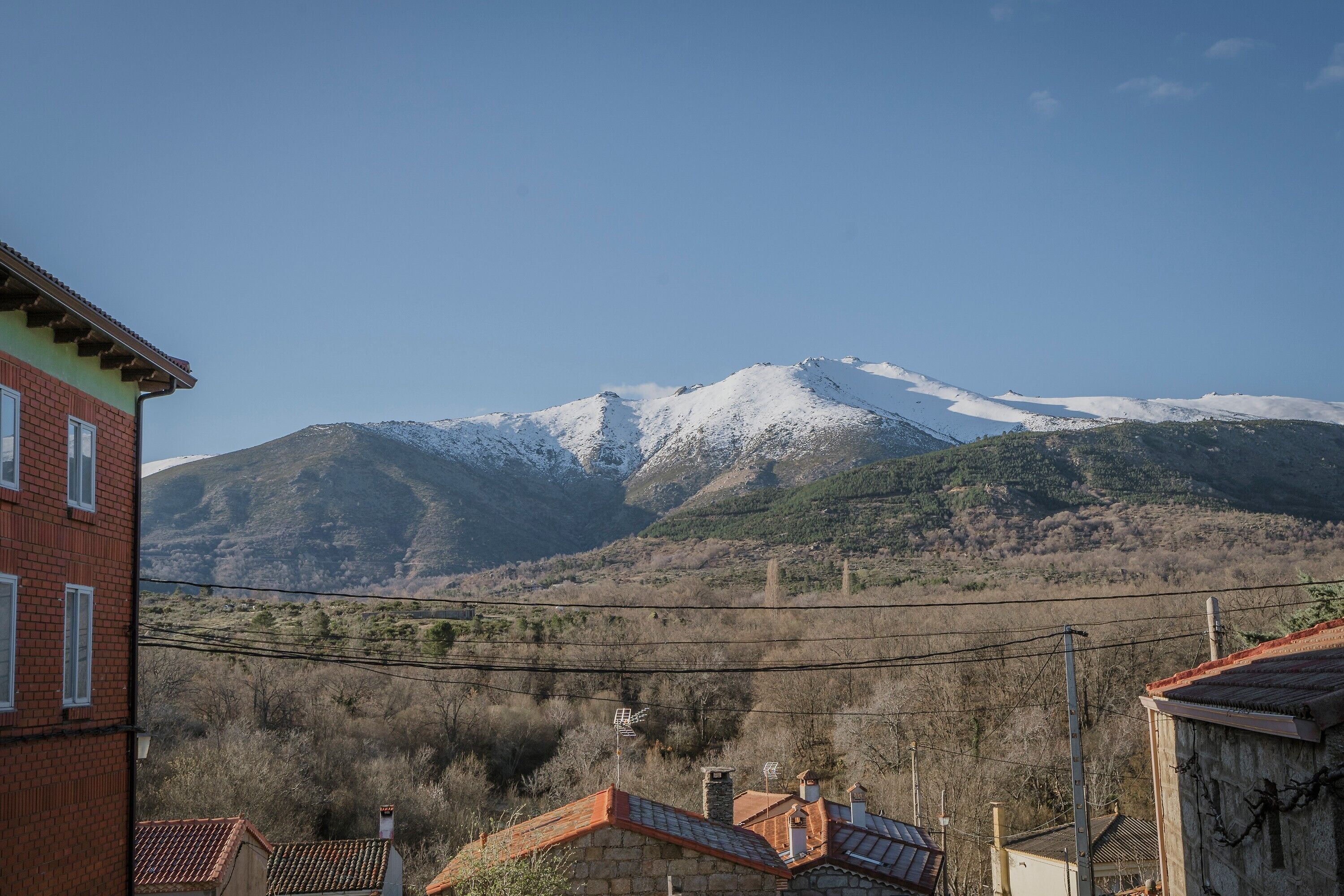 Uma montanha com picos nevados, céu claro e edifícios com telhados vermelhos em primeiro plano.