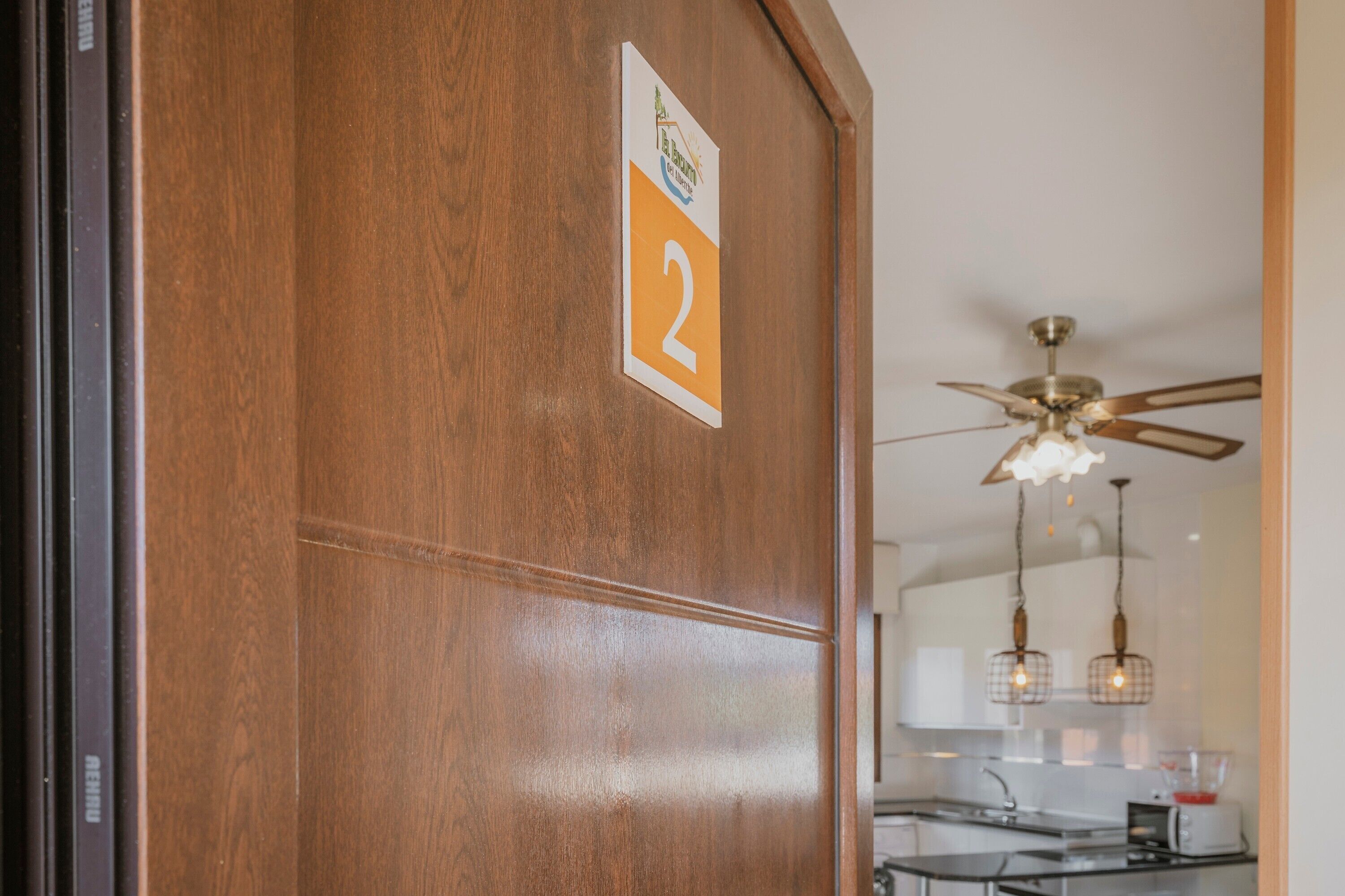 A wooden door with a number '2' sign, a ceiling fan, and a kitchen area with a microwave and sink.