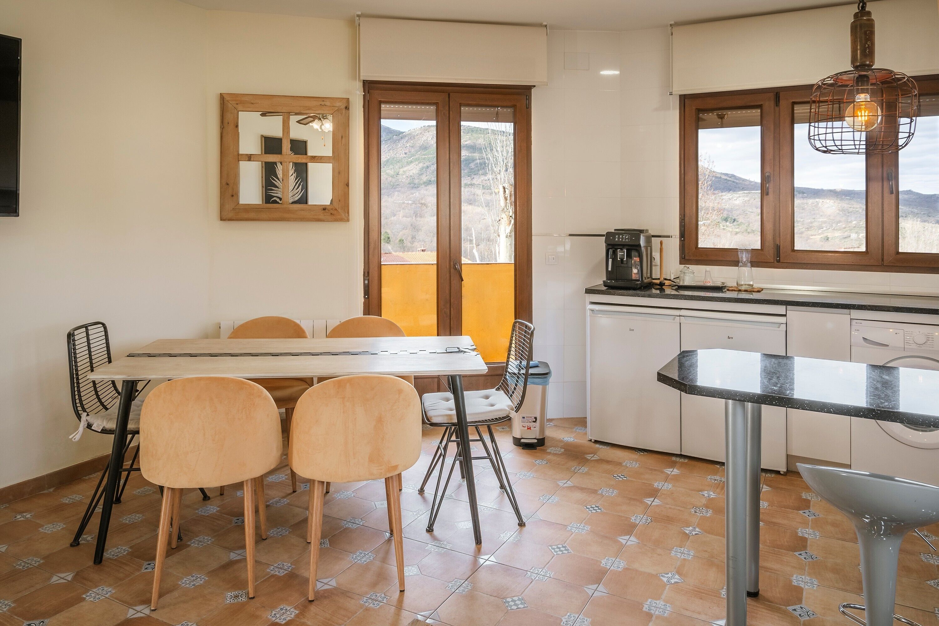 A kitchen with a dining table, chairs, a coffee machine, and a view of the outdoors.