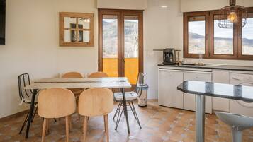 A kitchen with a dining table, chairs, a coffee machine, and a view of the outdoors.