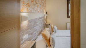 Un dormitorio con cabecera de madera, una mesita de noche y una cama con ropa de cama blanca y almohadas estampadas.