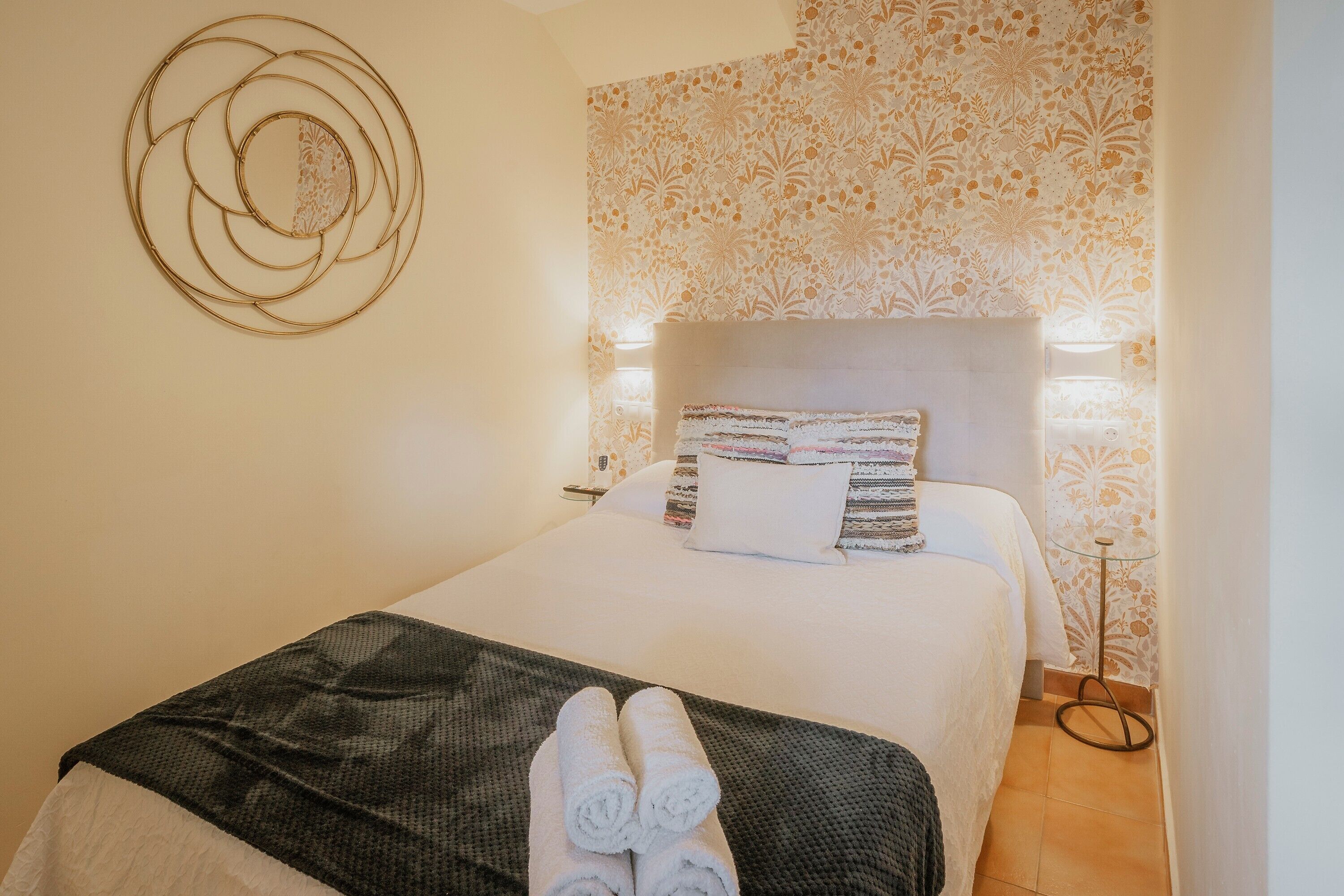 Una habitación de hotel con una cama, una obra de arte en la pared, papel tapiz estampado y una mesita de noche con una lámpara.