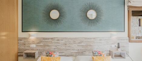 A hotel room with two beds, a large wall-mounted mirror, and a stone-patterned wall.