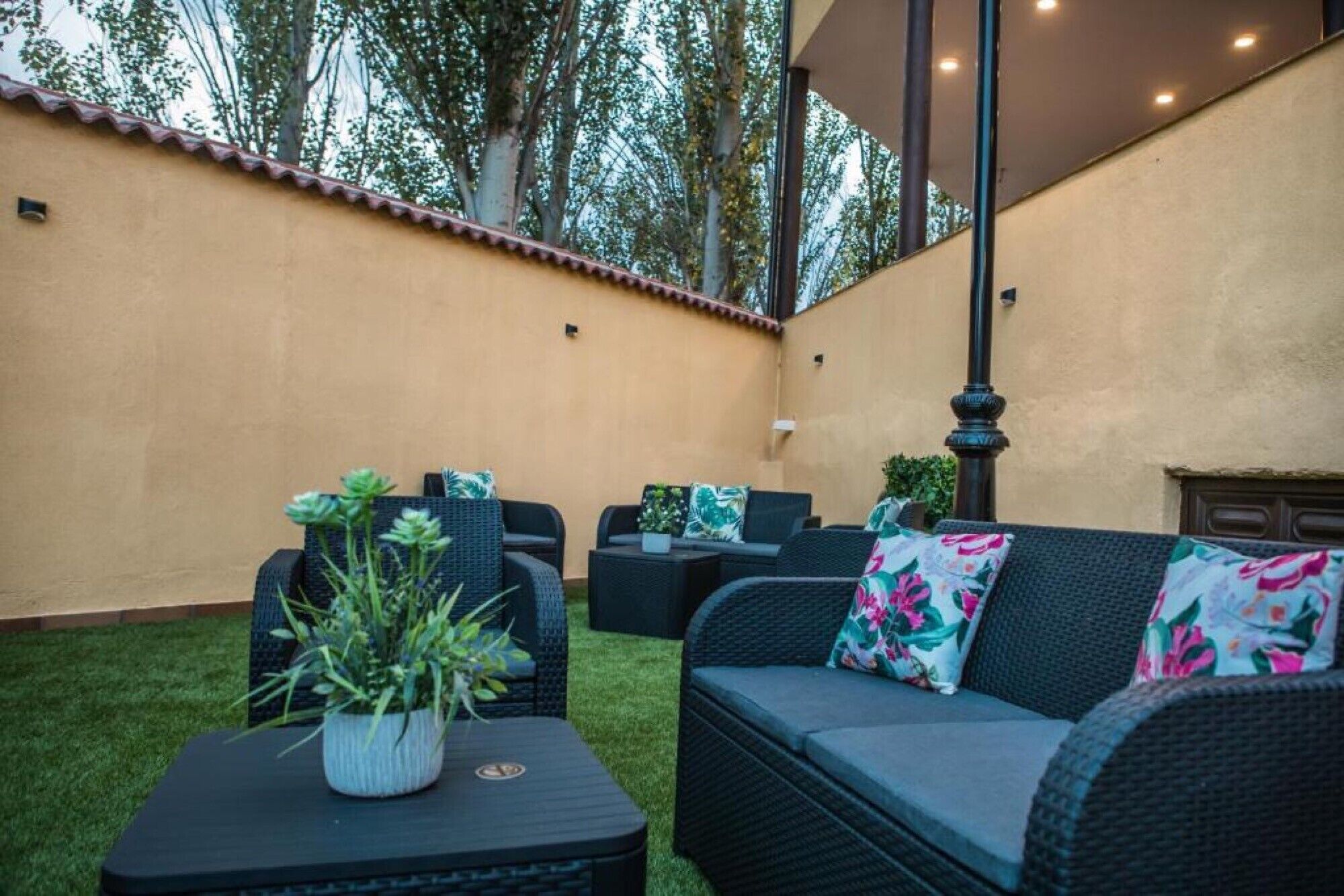 An outdoor patio with wicker furniture, a small table with a plant, and a decorative pillar.