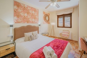 A hotel room with a bed, a ceiling fan, a window, a chair, and a table.