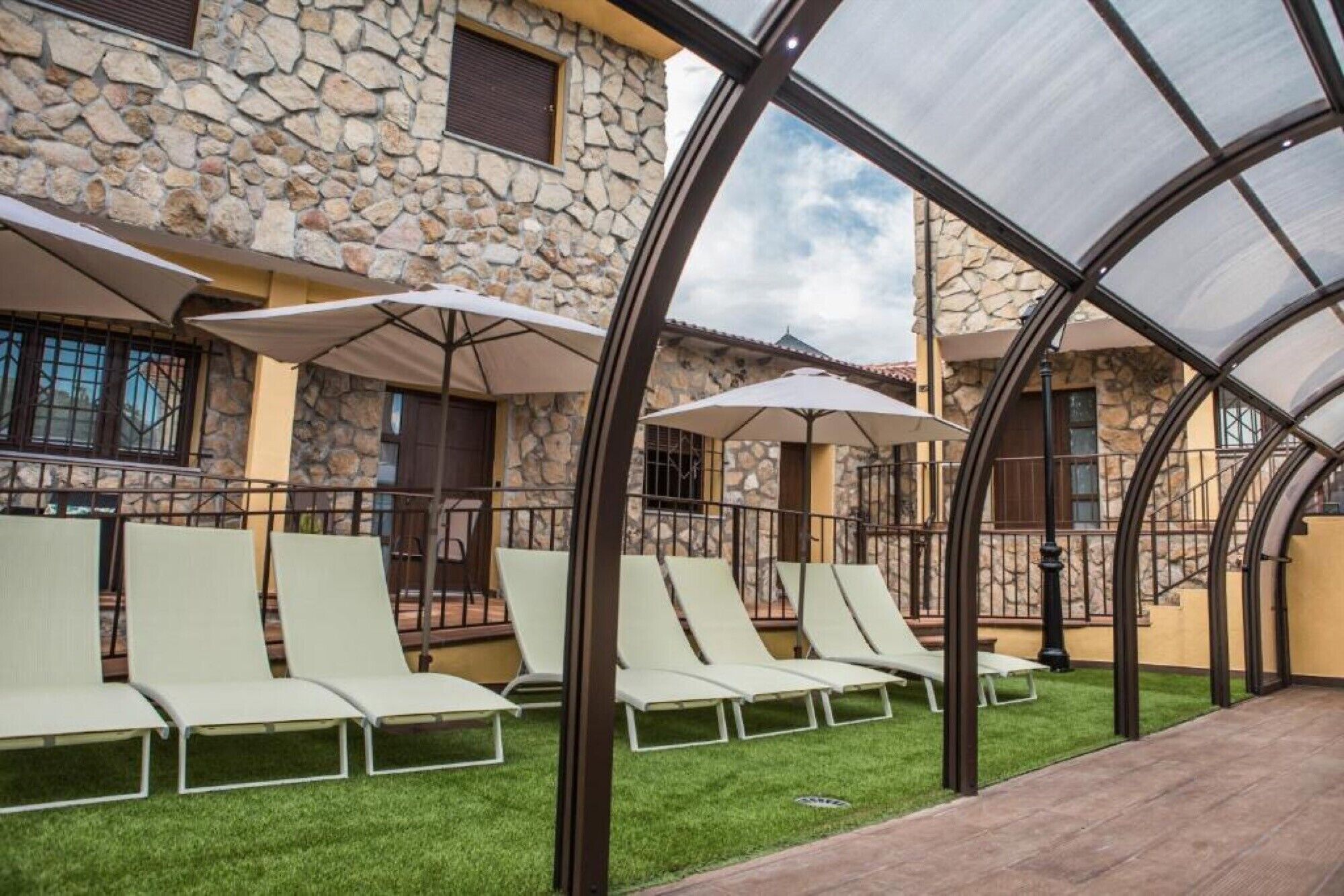 Een overdekt terras met lounge stoelen en parasols, muren van een stenen gebouw en een heldere lucht.