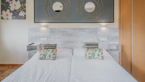 A double bed with floral-patterned pillows, a gray headboard, and a wall-mounted circular mirror.