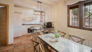 A modern kitchen with white cabinets, a marble dining table, and a hanging light fixture.