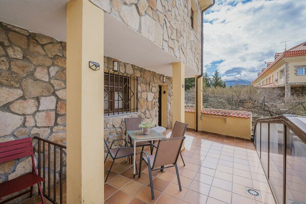 A balcony with stone walls, a table with chairs, and a bench.