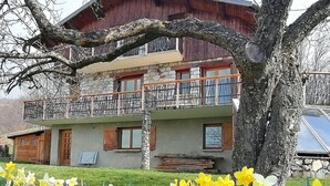 Ein zweistöckiges Gebäude mit Balkon, Steinmauern und einem Baum davor.