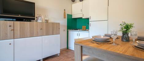 Una cocina moderna con televisor de pantalla plana, armarios blancos, una mesa de comedor con sillas y un salpicadero verde.