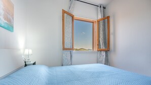 Un dormitorio con cama, mesita de noche, lámpara y ventana con cortinas.