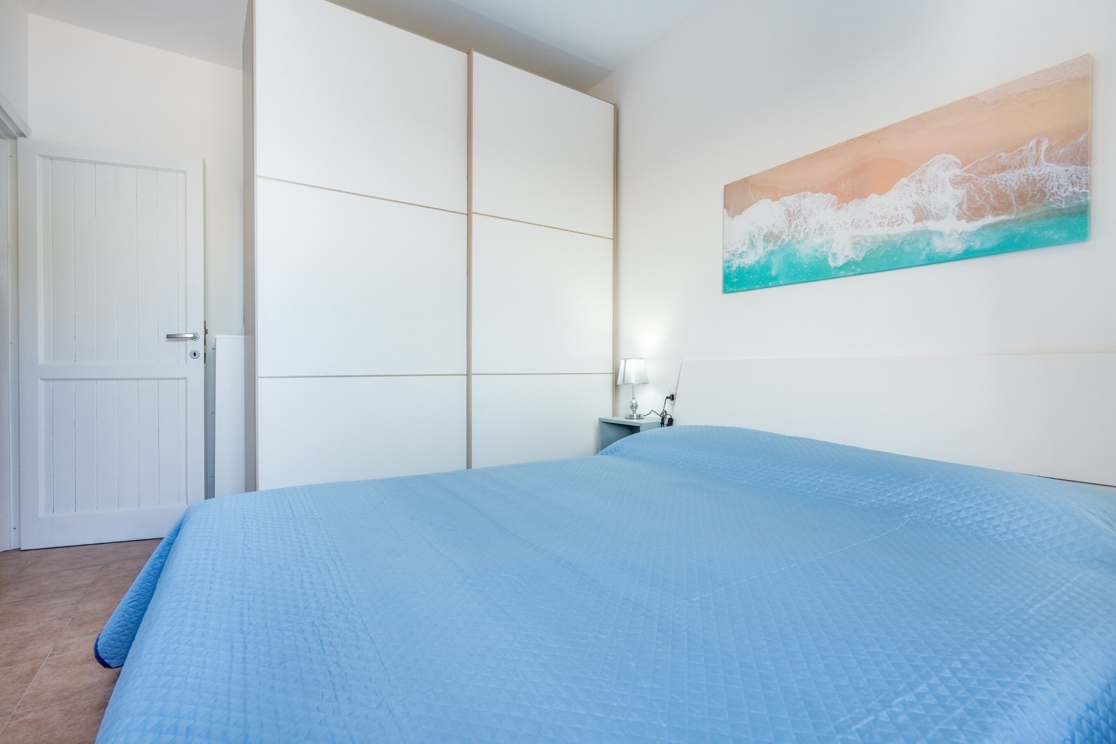 A bedroom with a bed, a nightstand, a painting, and a wardrobe.
