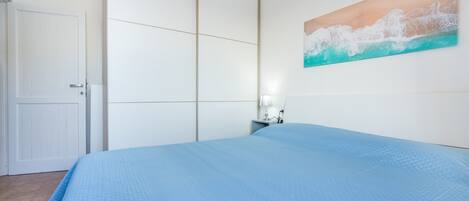 A bedroom with a bed, a nightstand, a painting, and a wardrobe.